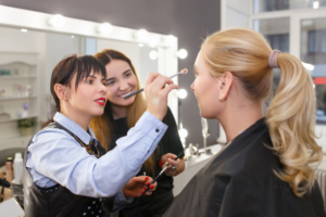 beauty school student practices applying makeup while instructor observes
