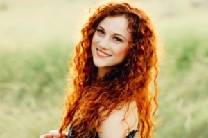 Collete Hood - An Nathan Layne Alumni portriat of her in a green grass field wearing a dress and red long curly hair