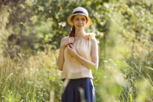 woman wearing vintage clothing and hat walking in a meadow